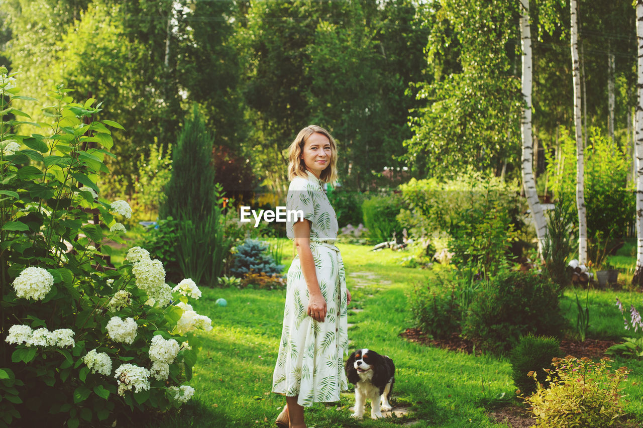 Portrait of smiling woman standing with dog against trees