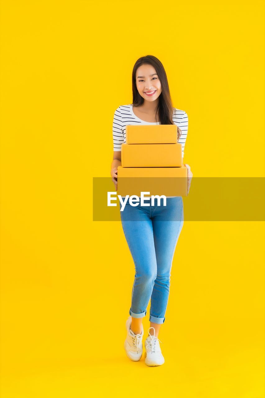 PORTRAIT OF A SMILING YOUNG WOMAN AGAINST YELLOW COLORED BACKGROUND