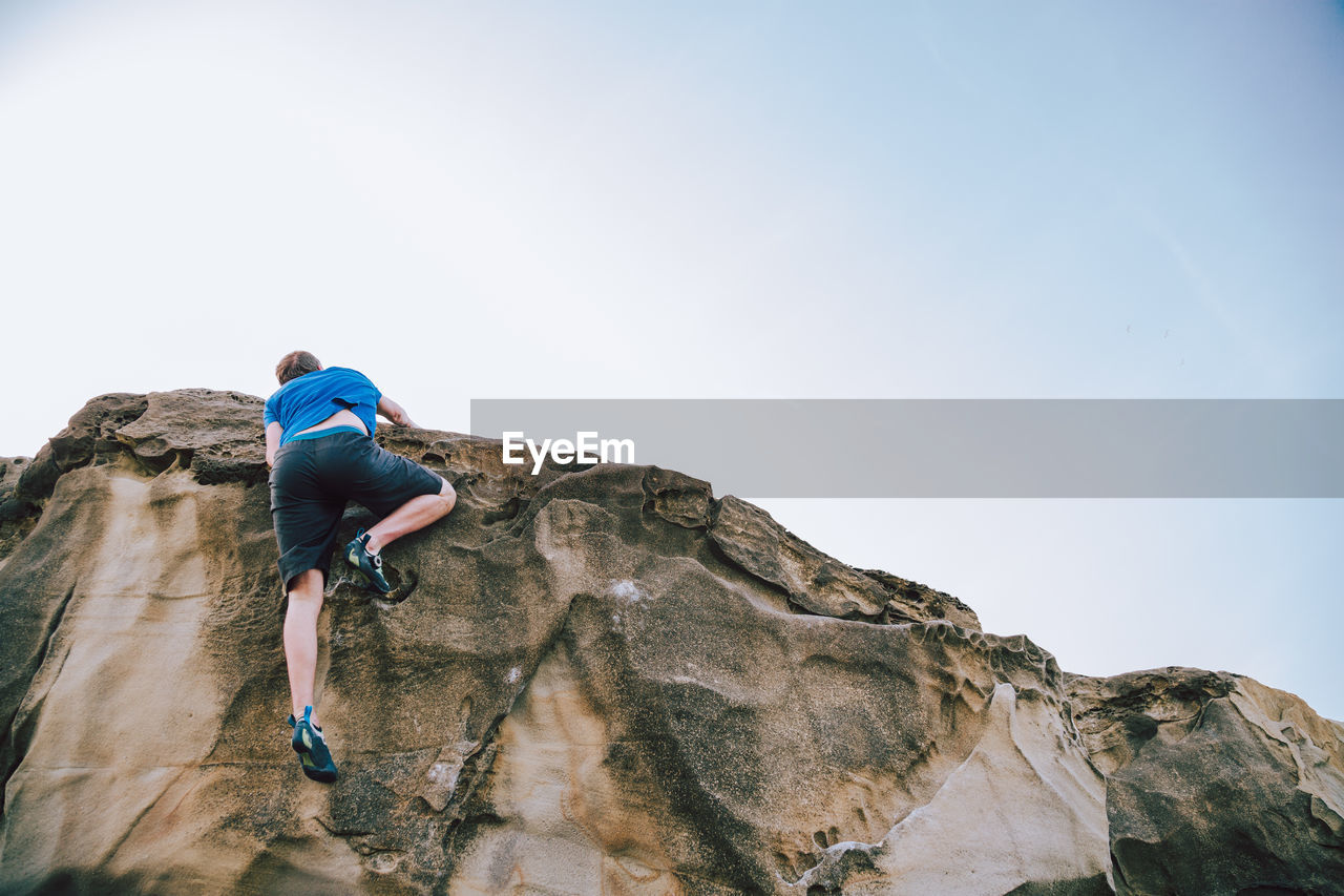 Man climbing on rock formation against sky