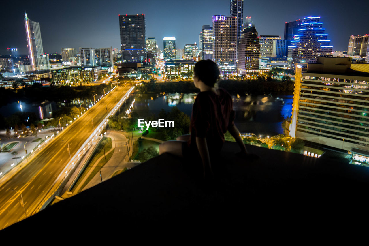 Girl on terrace looking at illuminated cityscape