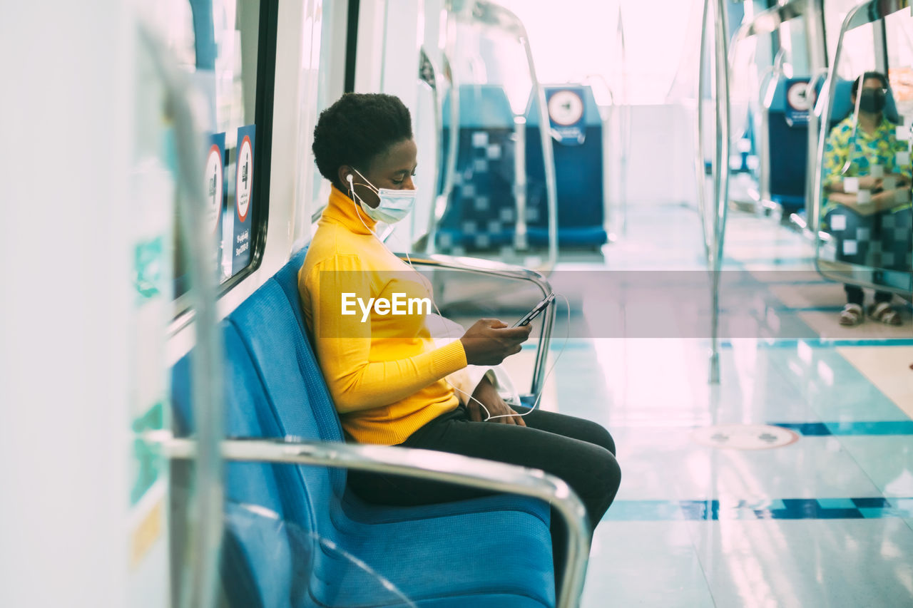 A young african woman in a protective mask rides the subway and listens to music with headphone