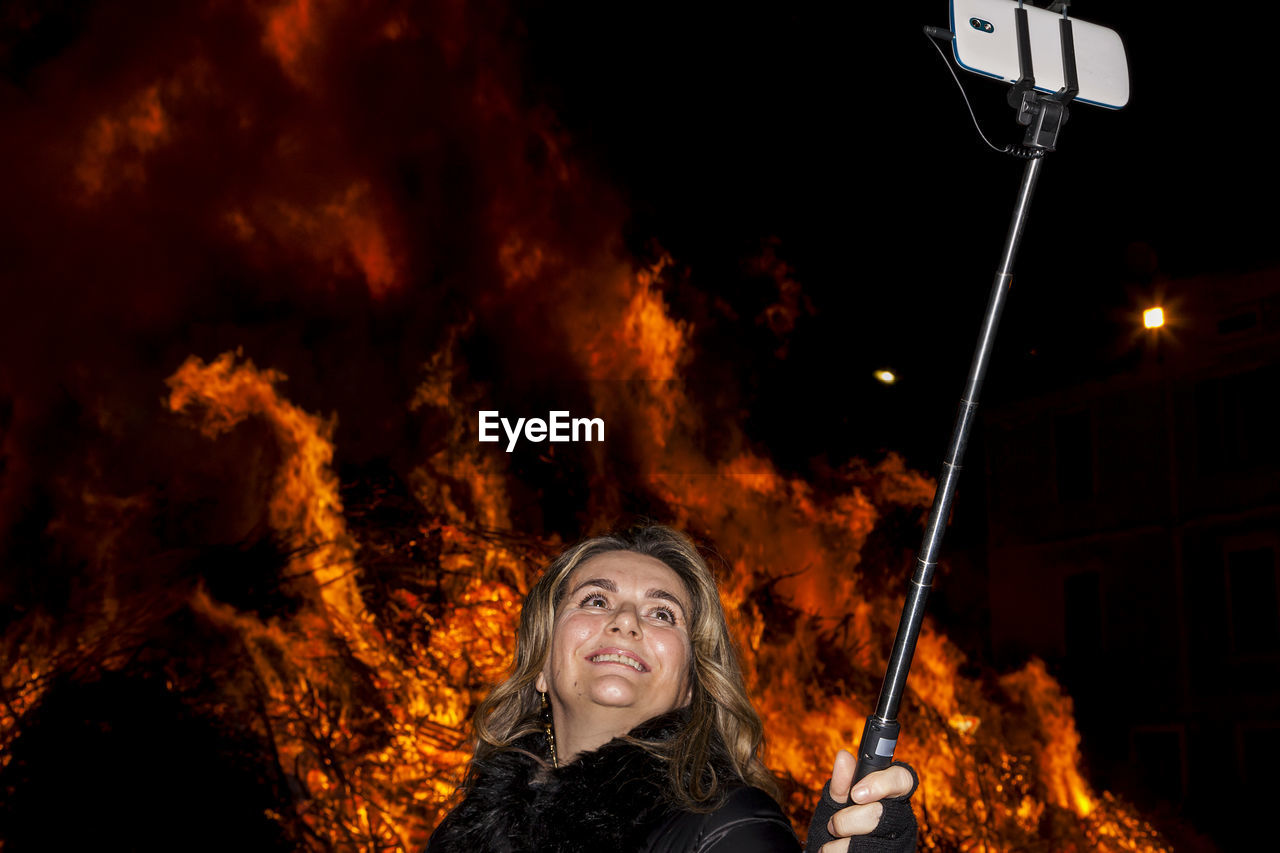 Woman taking selfie against bonfire at night