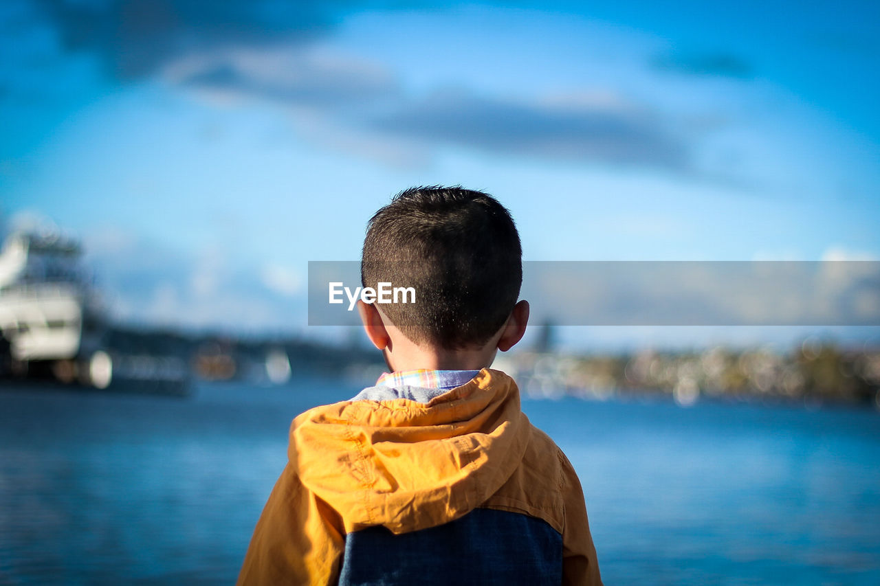 Rear view of boy standing in sea against sky