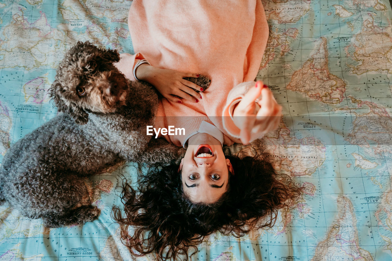 High angle portrait of woman with dog lying on bed at home