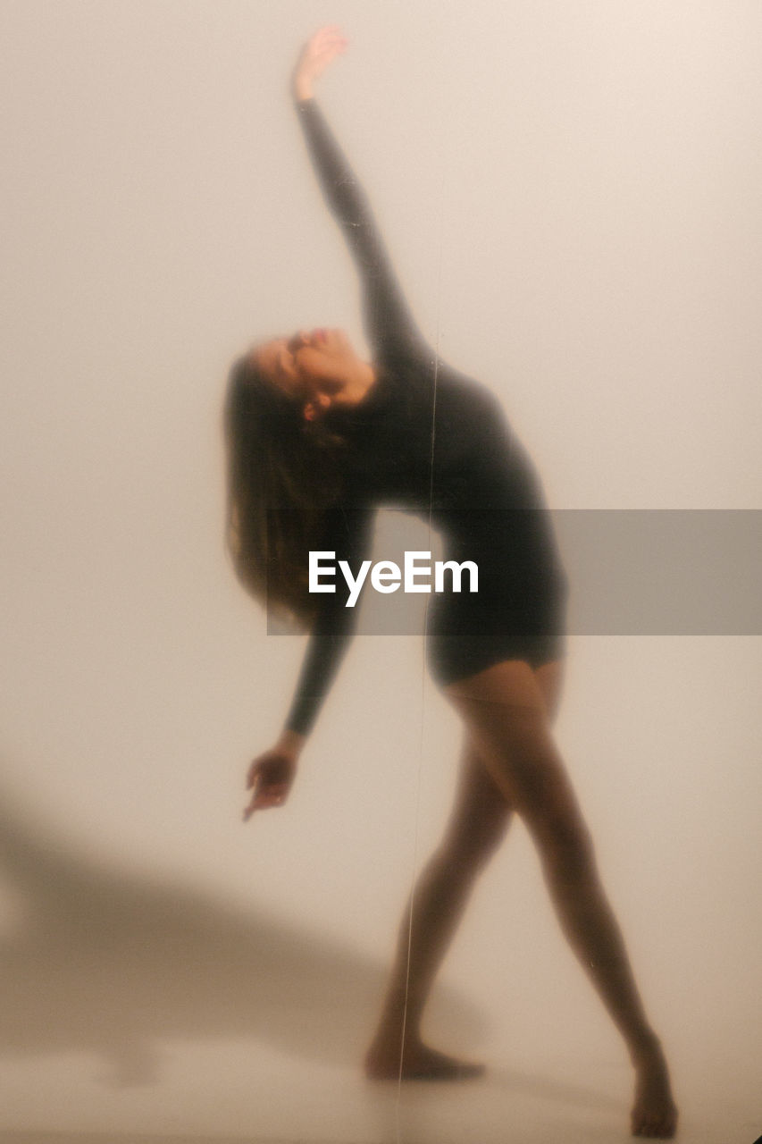 Full body of slim barefoot blurred female dancer with long hair in black wear dancing on white background in studio