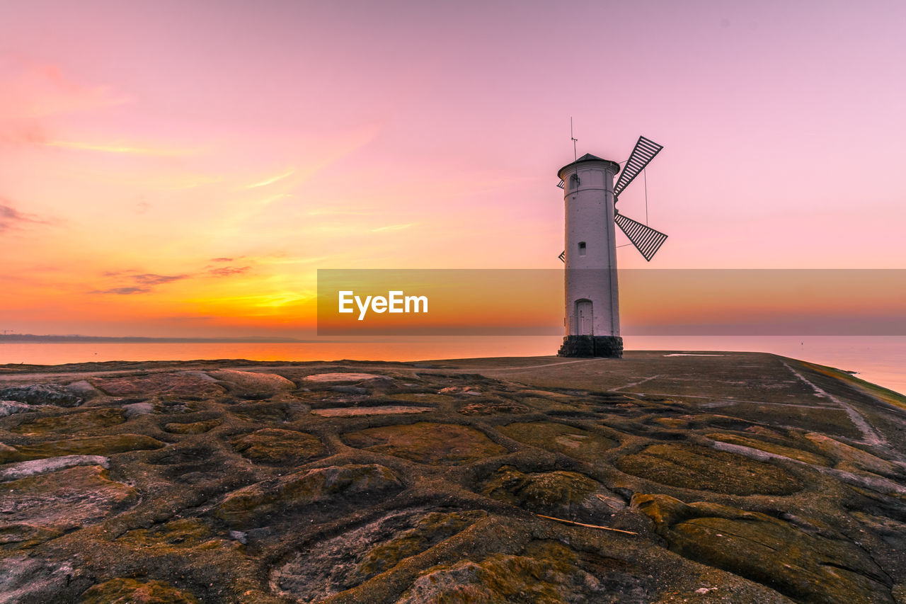 Lighthouse by sea against sky during sunset