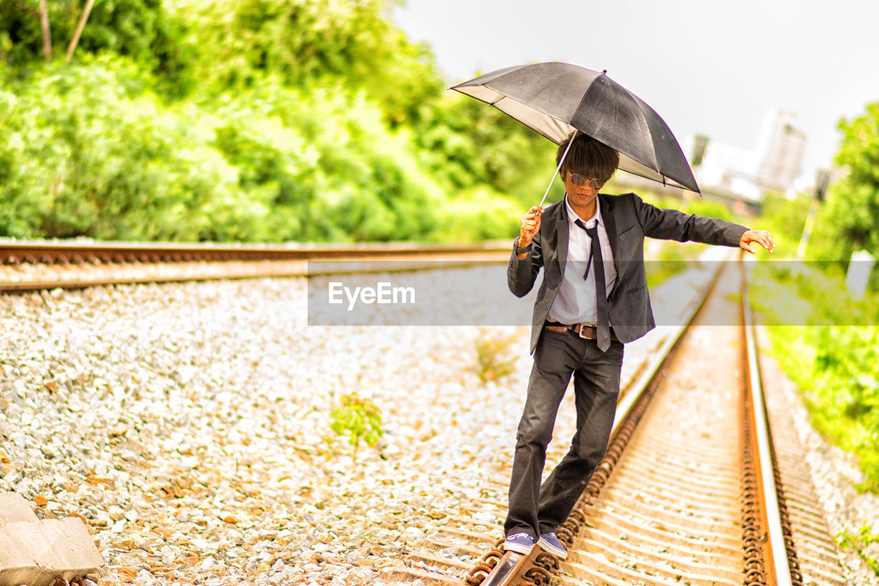 Businessman with umbrella walking on railroad track