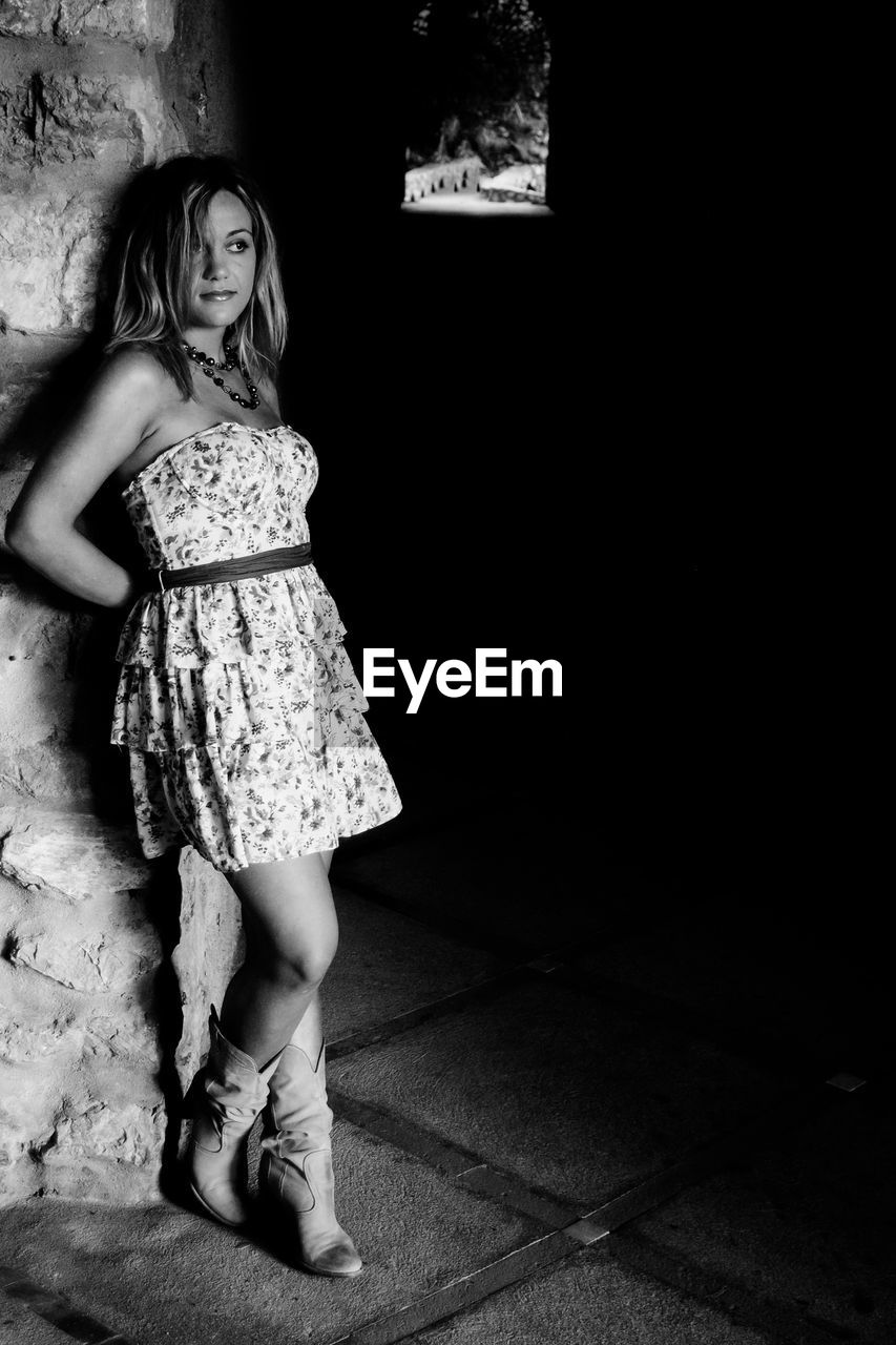 Black and white portrait of young woman leaning against wall at the entrance of a tunnel