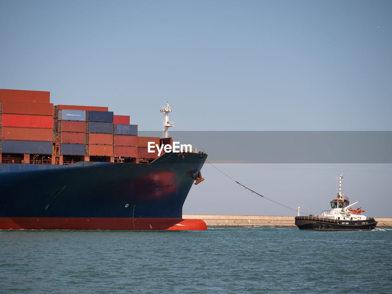 Large container ship towed into port by a small tugboat.