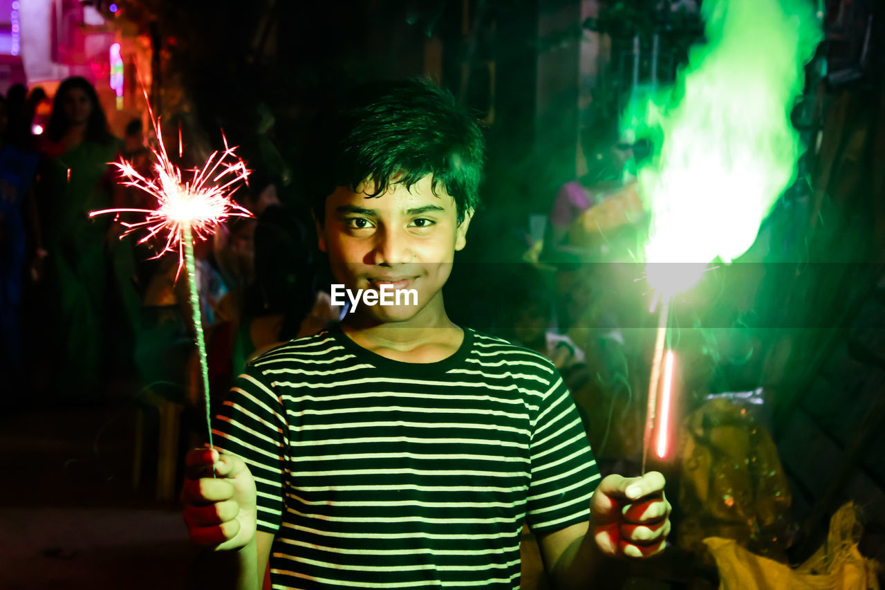 Portrait of teenage boy holding sparklers at night