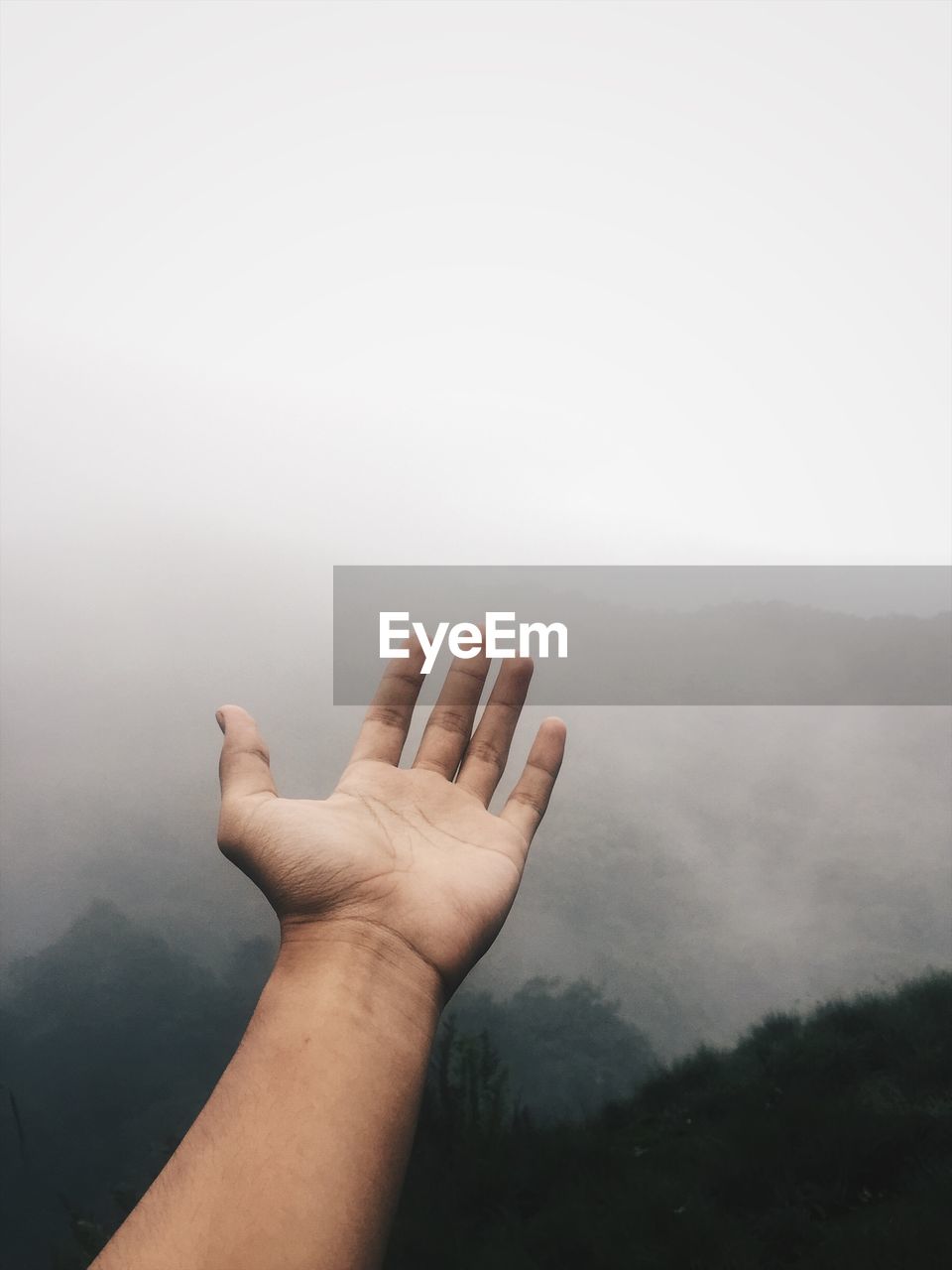 Cropped hand of man gesturing against mountains during foggy weather