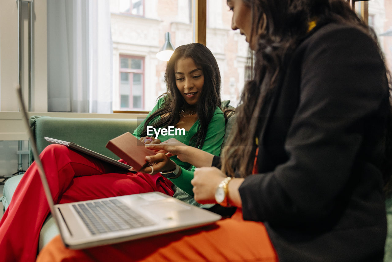 Female business colleagues discussing over box while sitting at workplace