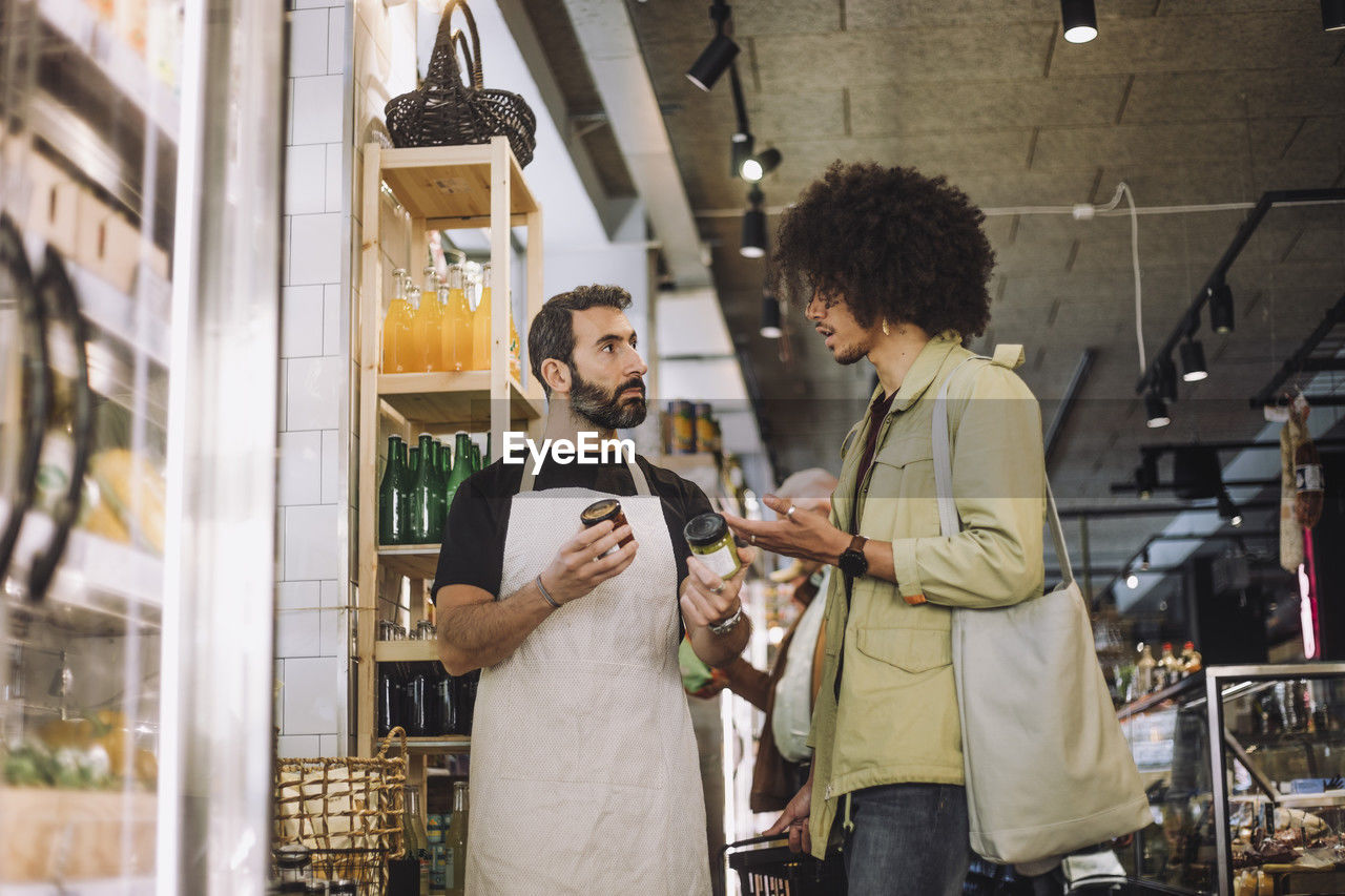 Salesman and young male customer discussing over jars at grocery convenience store