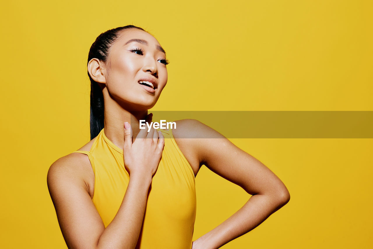 portrait of young woman standing against yellow background