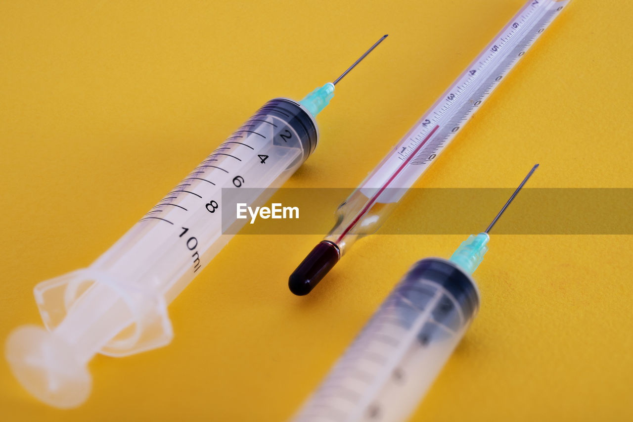 High angle view of syringes and thermometer on yellow background