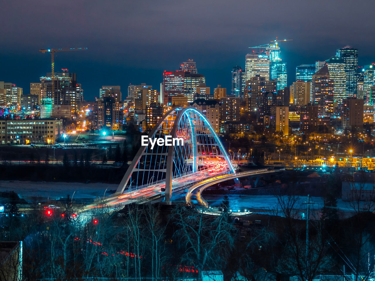 ILLUMINATED BRIDGE OVER BUILDINGS AGAINST SKY AT NIGHT