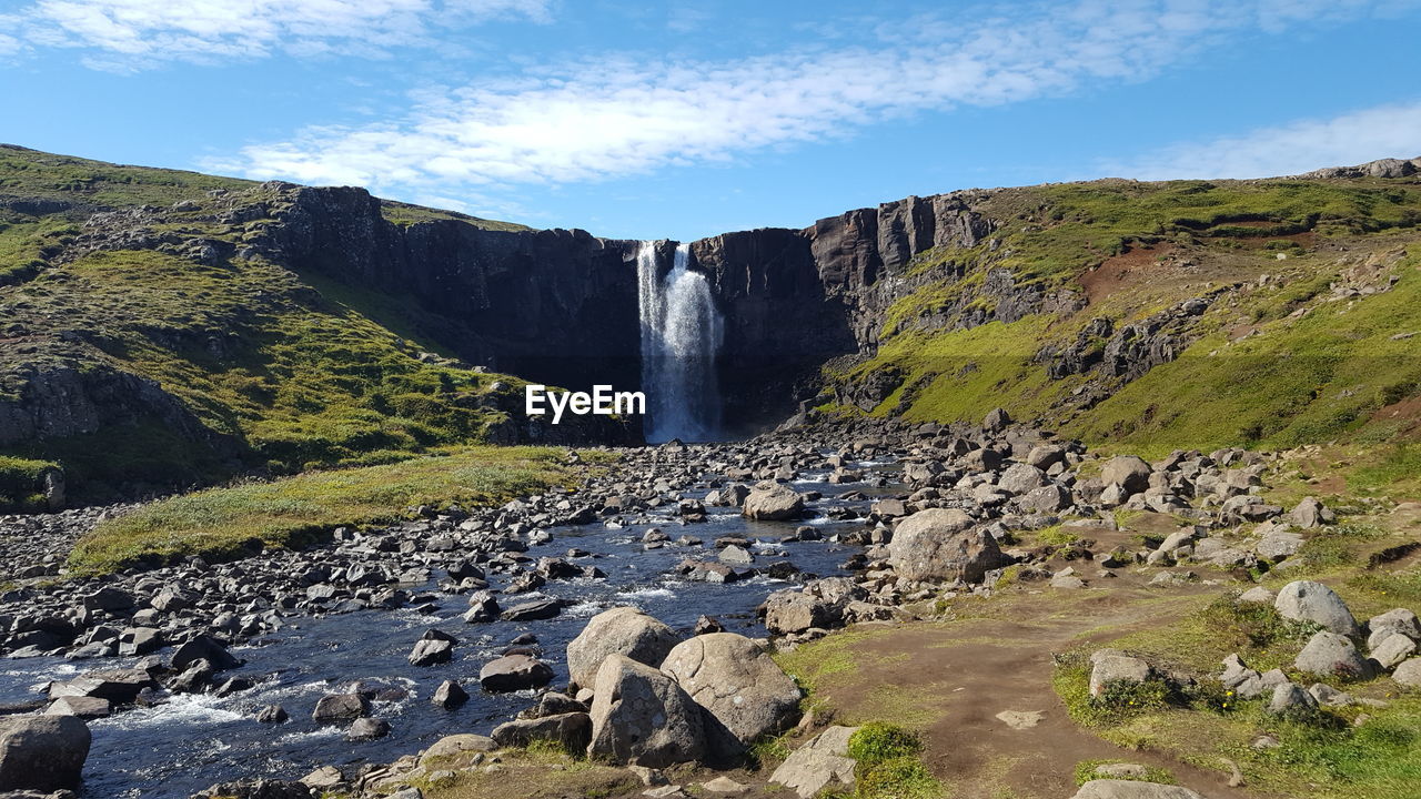 SCENIC VIEW OF WATERFALL BY MOUNTAINS AGAINST SKY