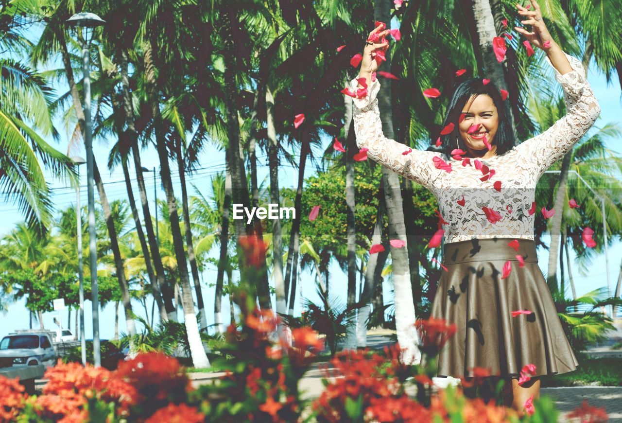 PORTRAIT OF SMILING WOMAN STANDING BY PLANTS