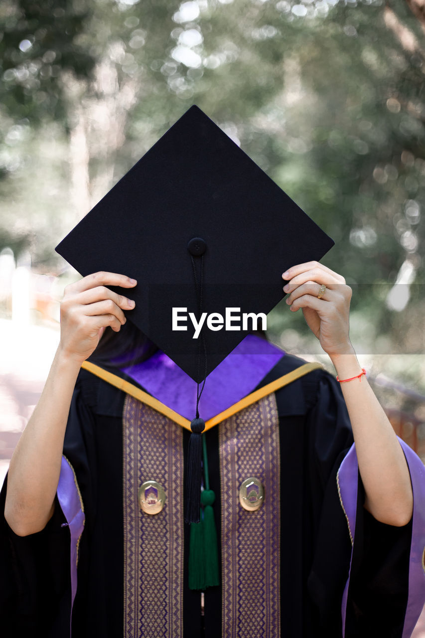 Woman wearing graduation gown holding mortarboard