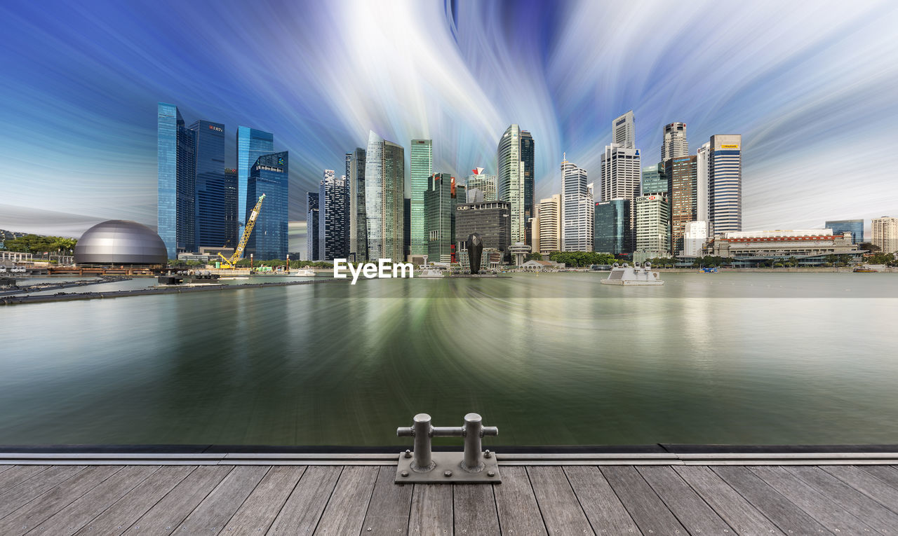 Modern buildings by river against sky in city