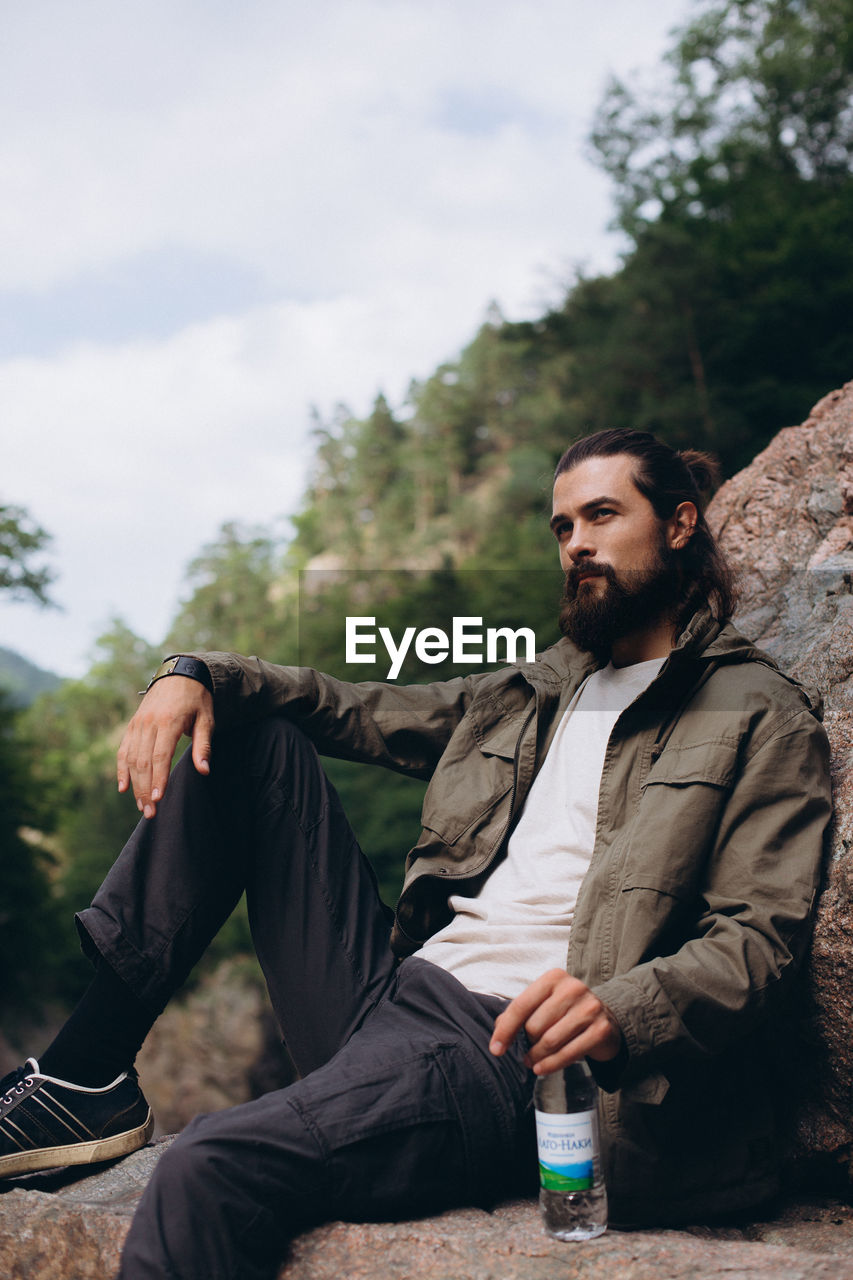 YOUNG MAN LOOKING AWAY WHILE SITTING ON TREE