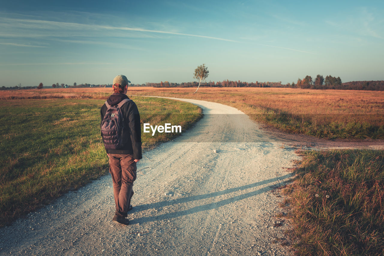 A man with a backpack goes gravel road on an autumn day