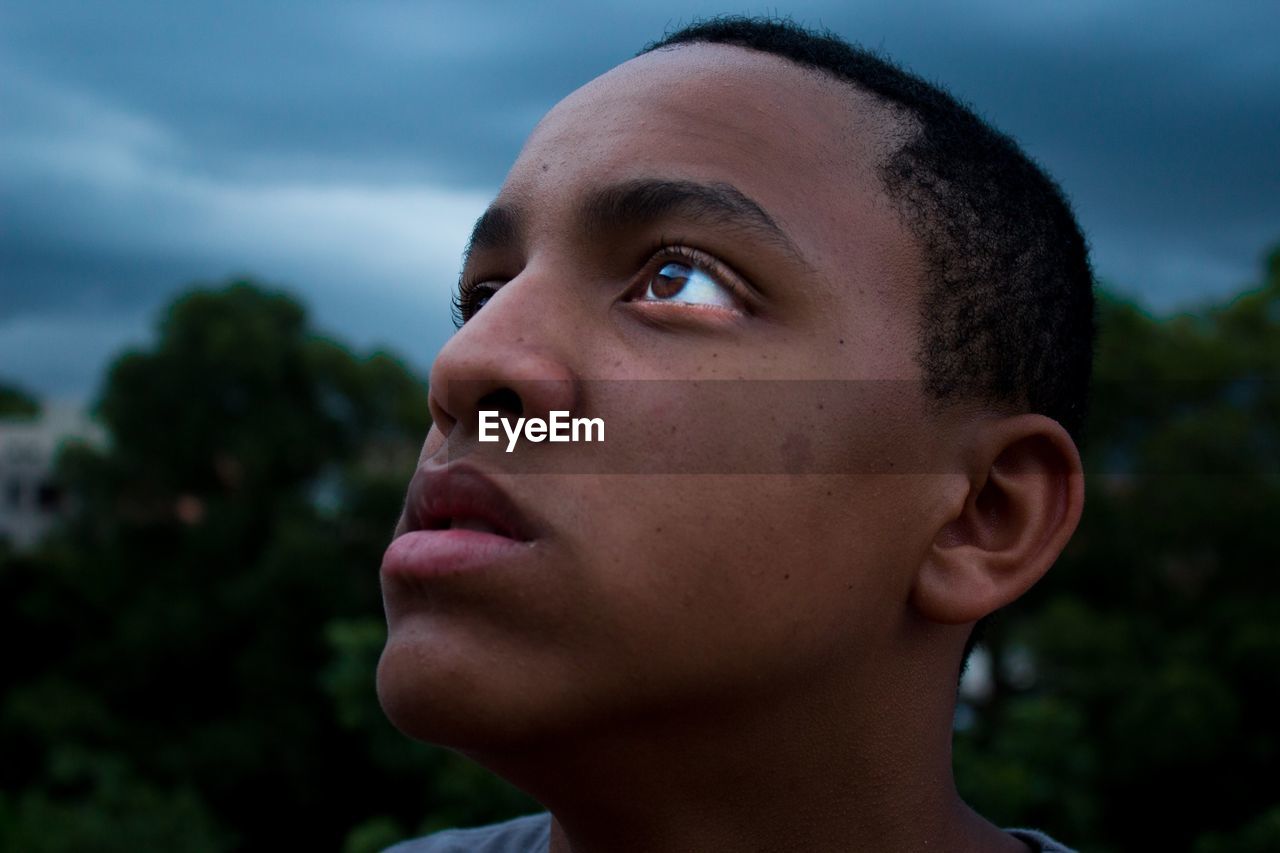 Close-up of teenage boy looking up against cloudy sky