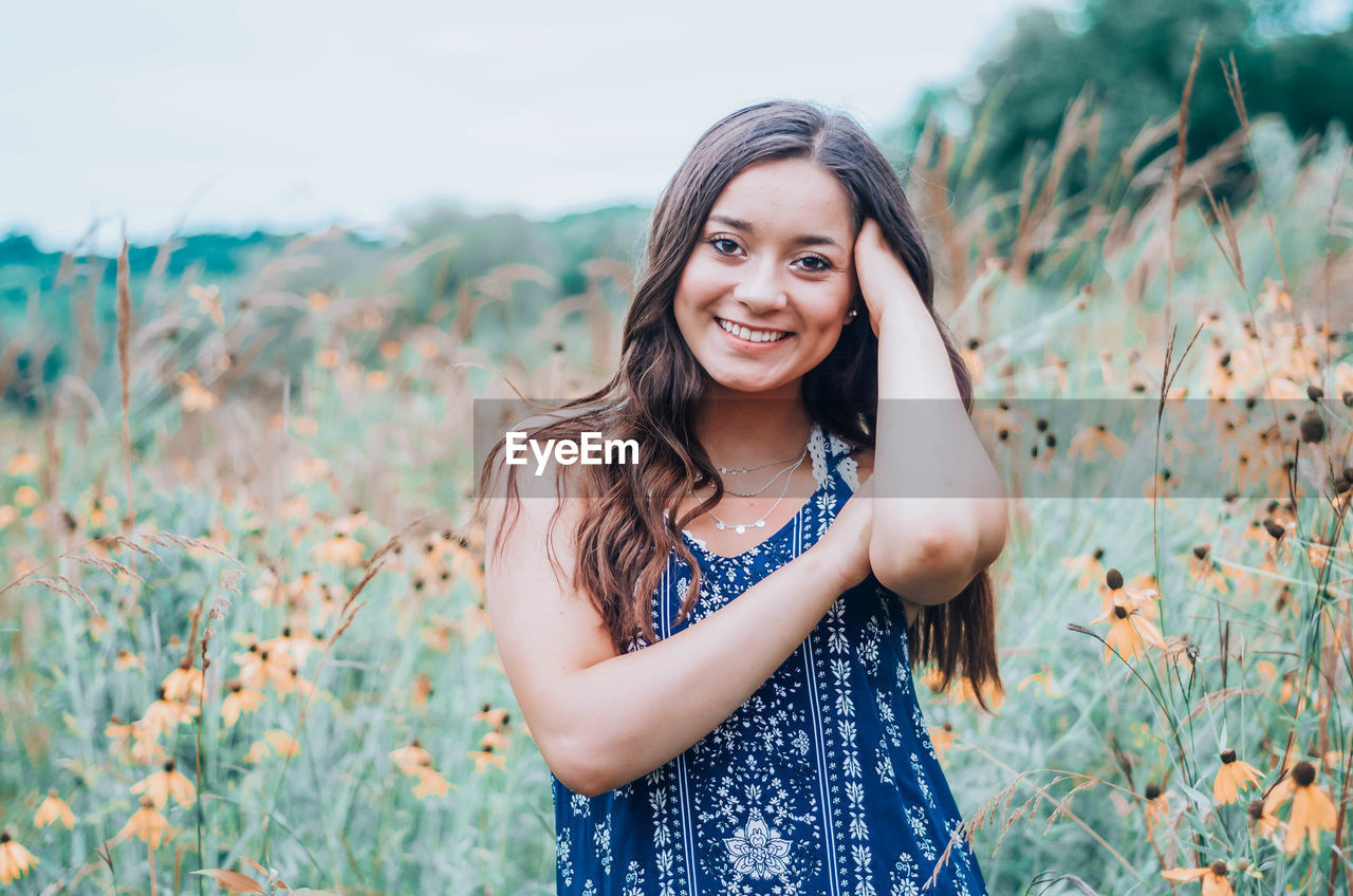 Portrait of smiling young woman standing on field against sky