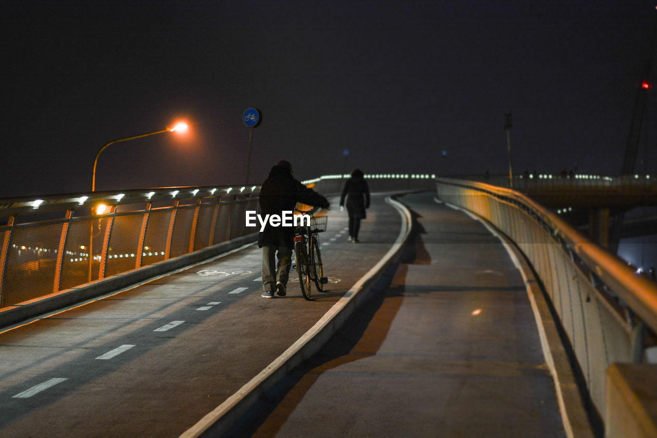 PEOPLE ON BRIDGE AGAINST ILLUMINATED STREET LIGHTS