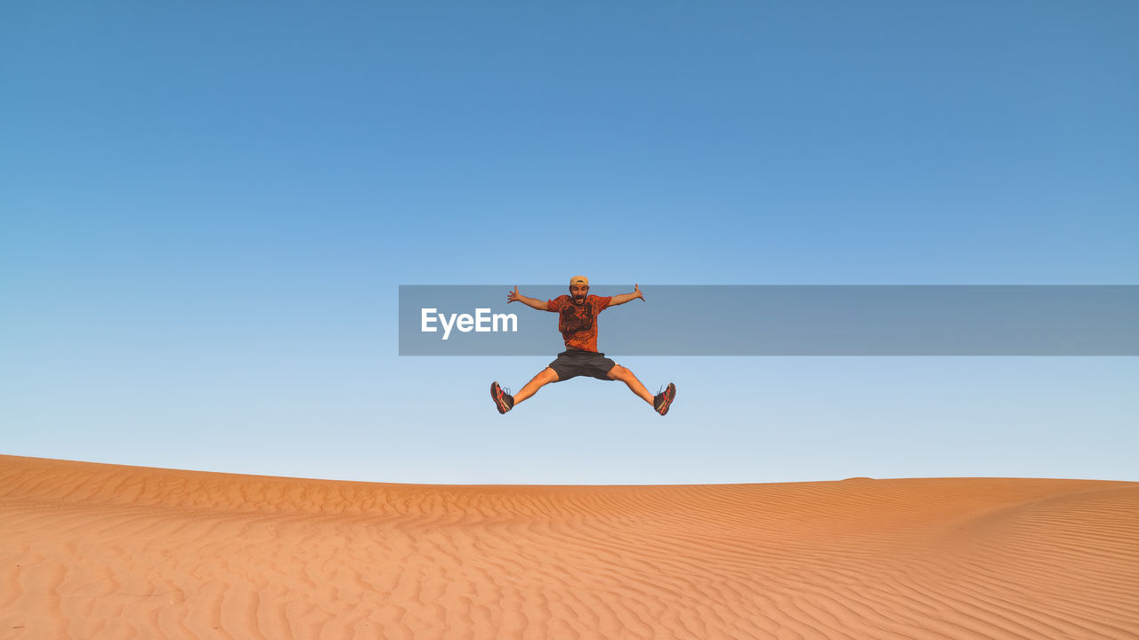 Man jumping in desert against clear sky