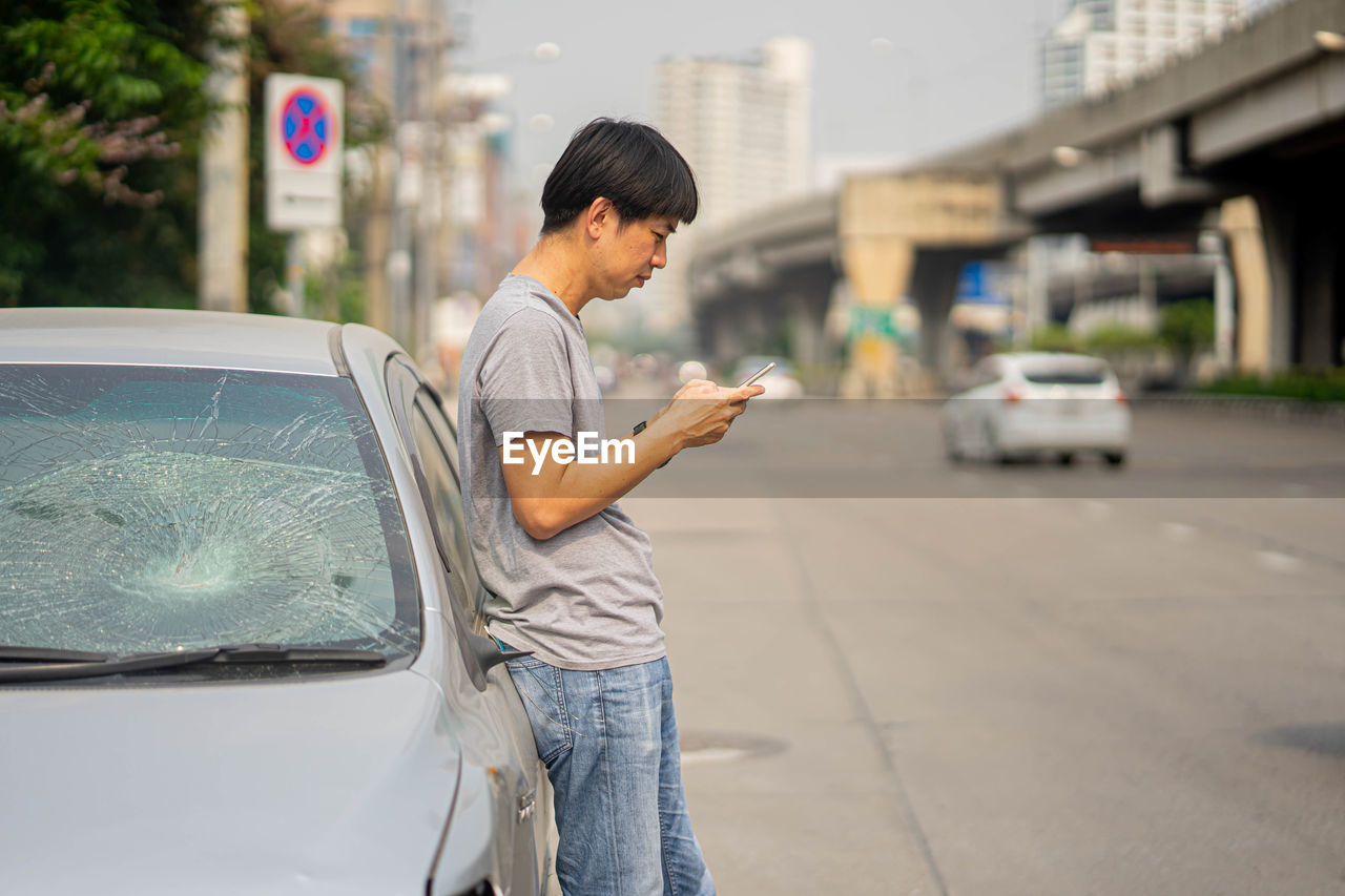 SIDE VIEW OF MAN USING SMART PHONE IN CITY