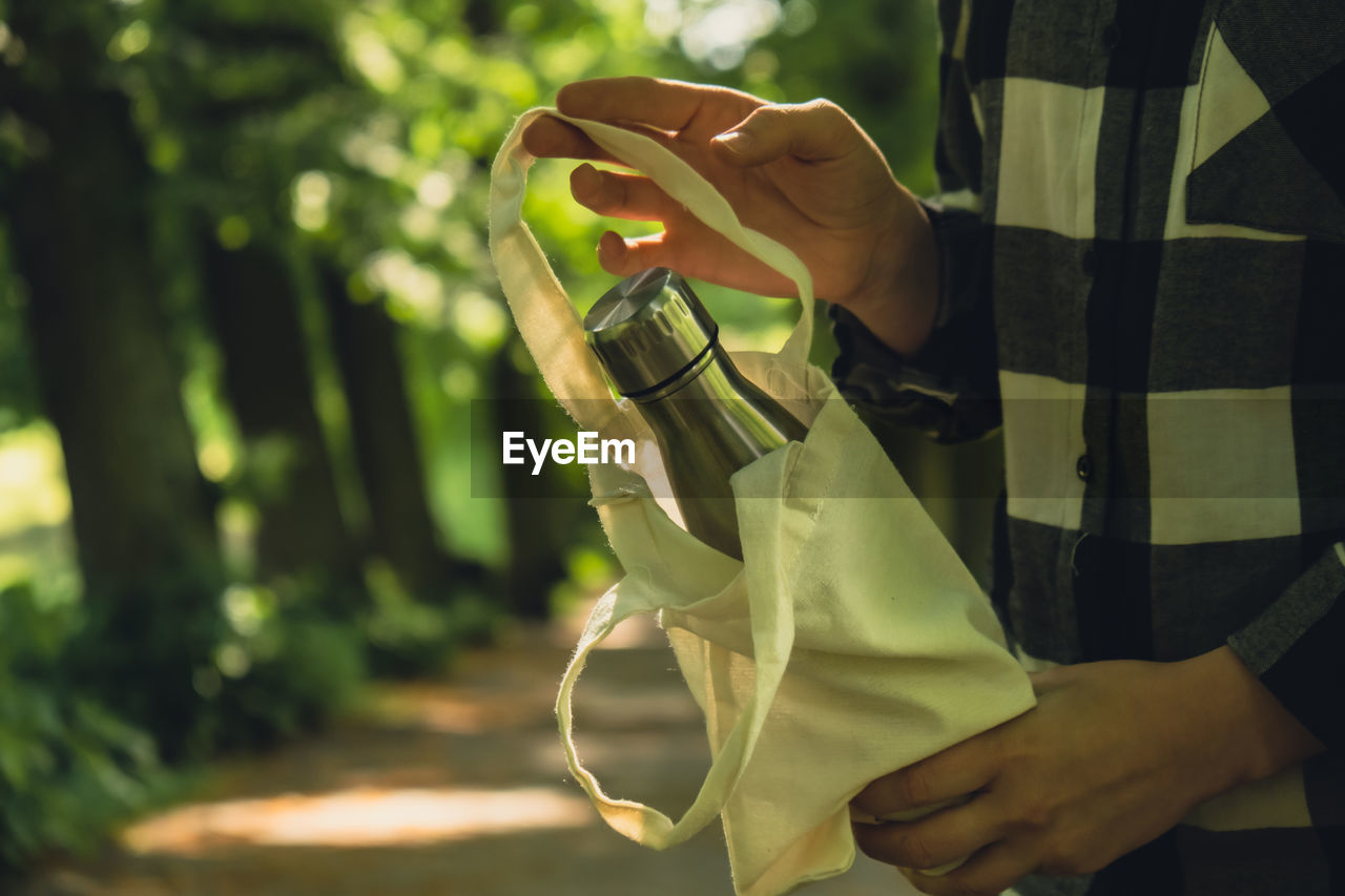 Close-up of unrecognizable female hand holding water bottle from eco bag. reusable steel thermo