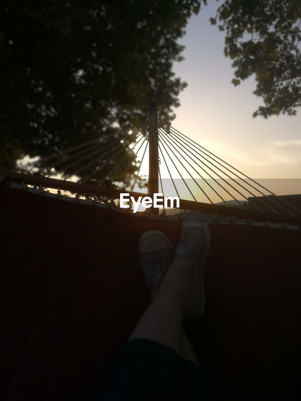LOW SECTION OF PERSON RELAXING IN HAMMOCK AGAINST SKY
