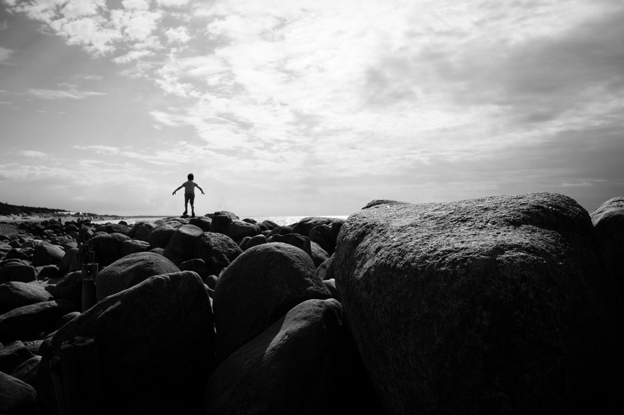 SILHOUETTE MAN STANDING AMIDST ROCKS AGAINST SKY