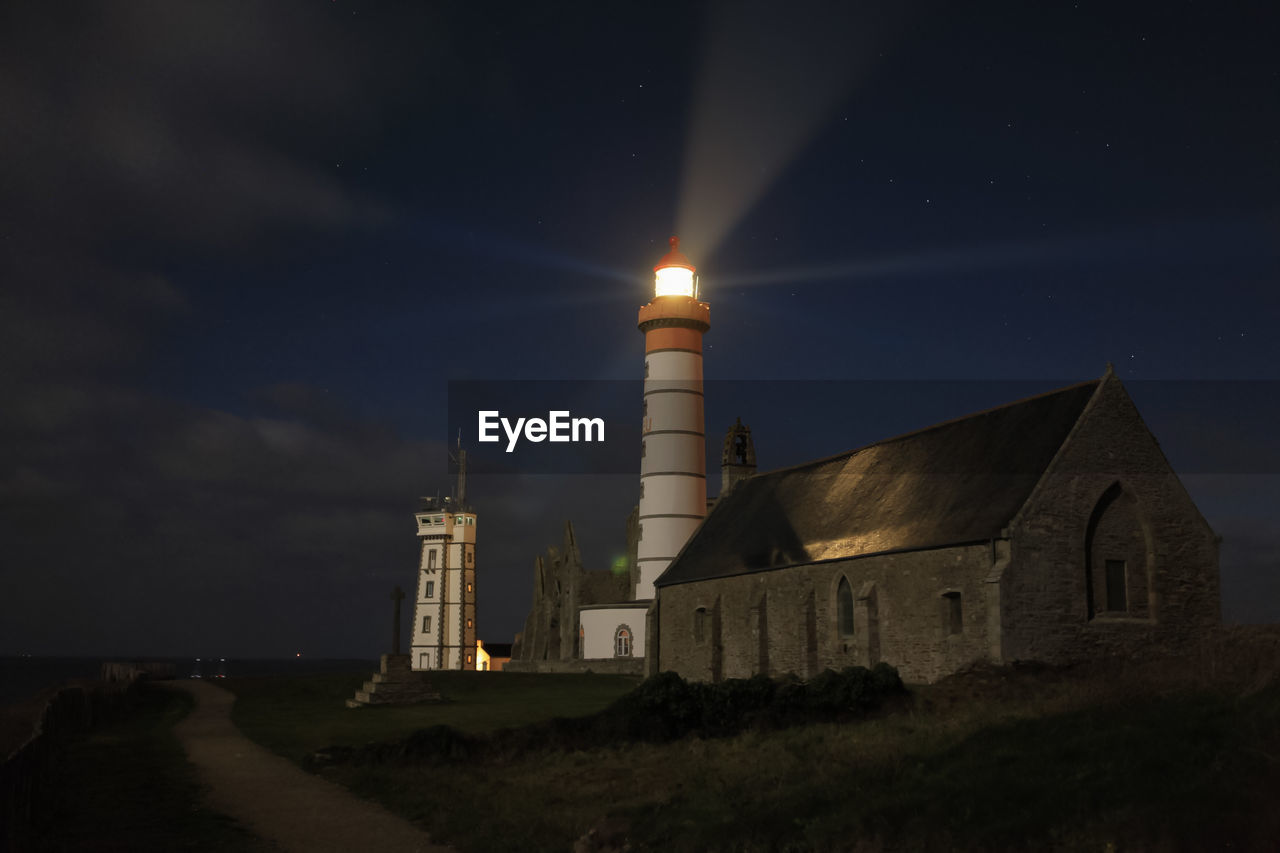 Illuminated lighthouse on field against sky at night