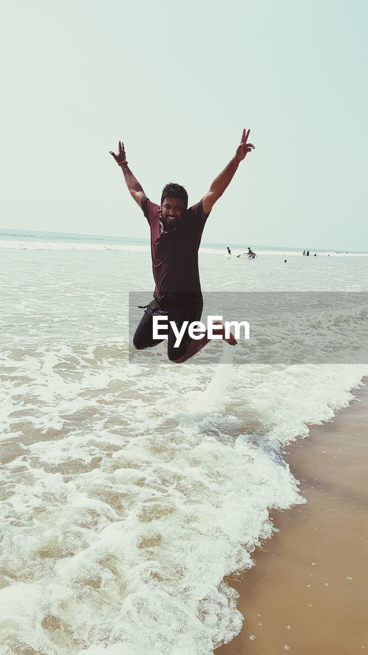 Man with arms raised jumping at beach