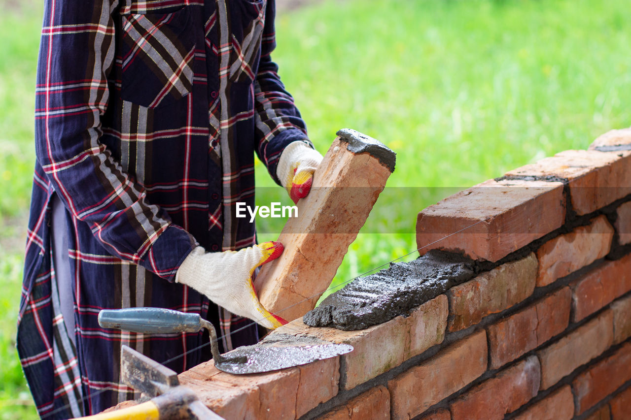 A young woman builds a brick wall, puts a brick on a cement-sand mortar
