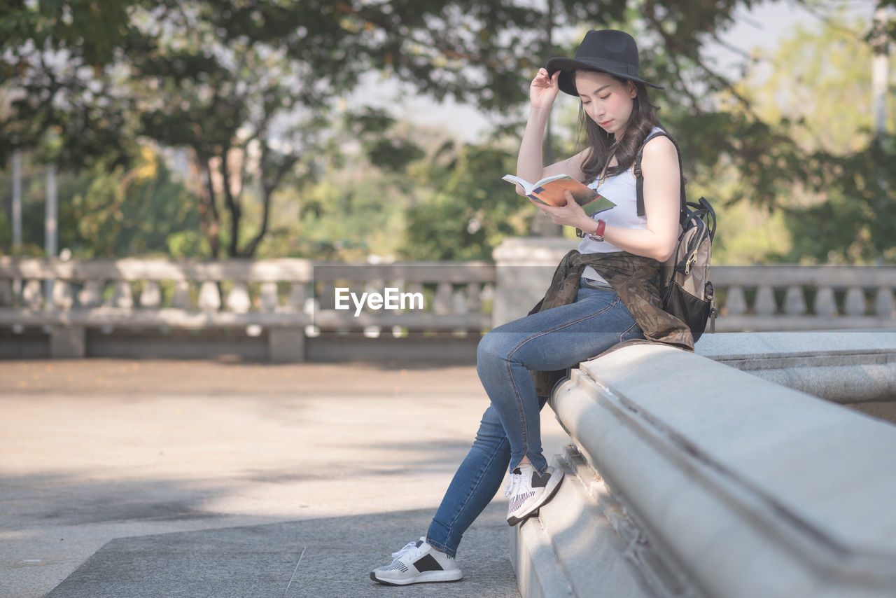 Full length of female tourist reading book while sitting in city