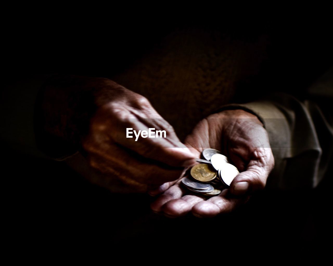 Close-up of cropped hands holding coins against black background