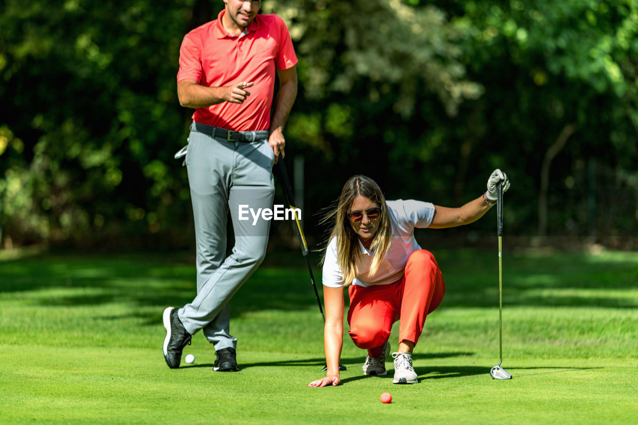 Couple playing golf, young woman reading green, getting ready to putt