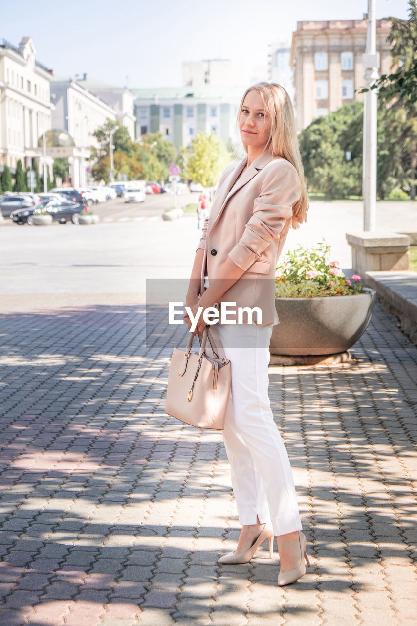 Portrait of a successful business woman with blonde long hair. in an expensive suit,fashionable bag.