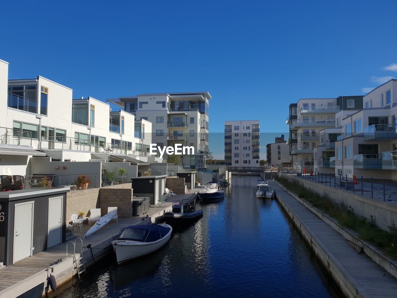 Boats in canal amidst buildings in city against clear blue sky