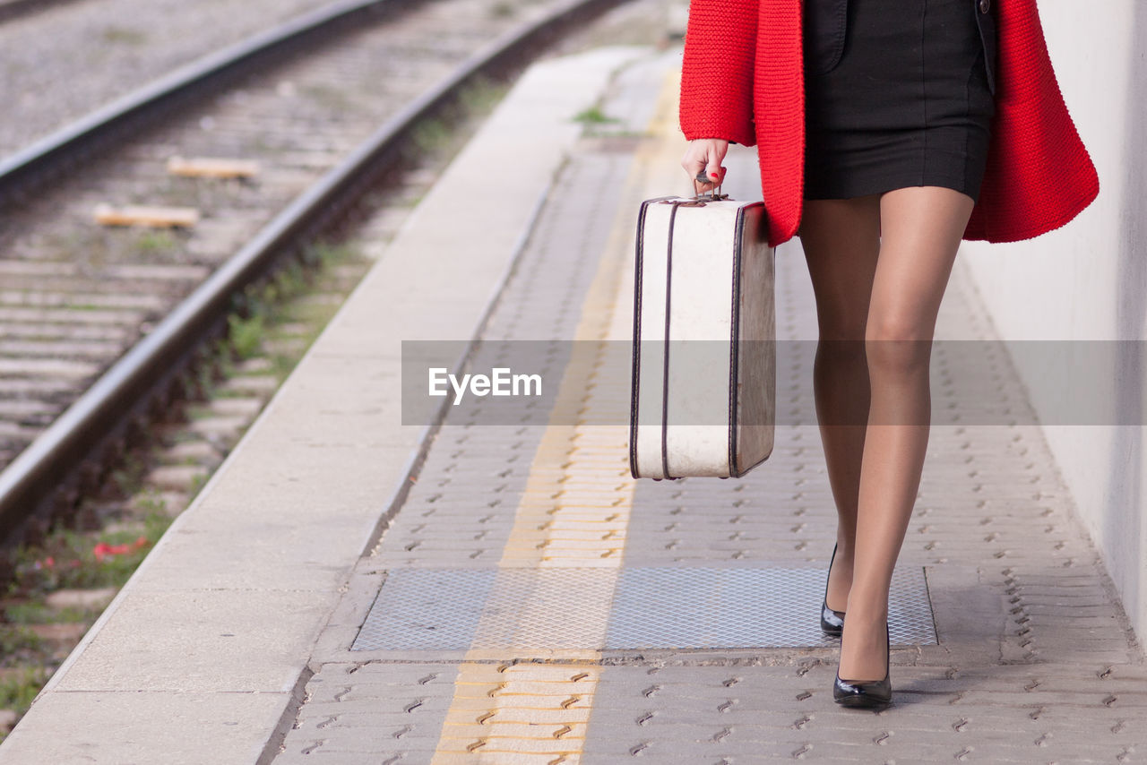 Low section of young woman with luggage walking on platform at station