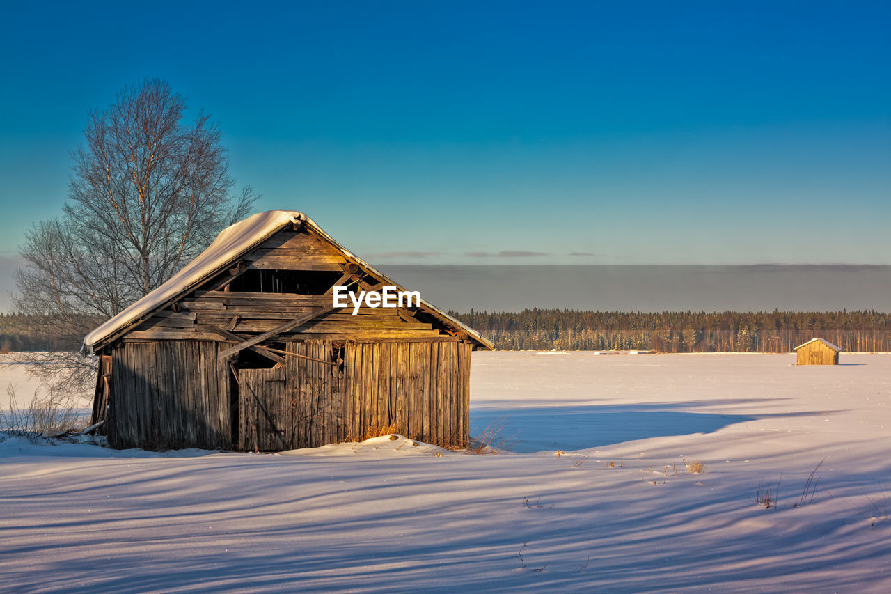 House on snow covered field against blue sky