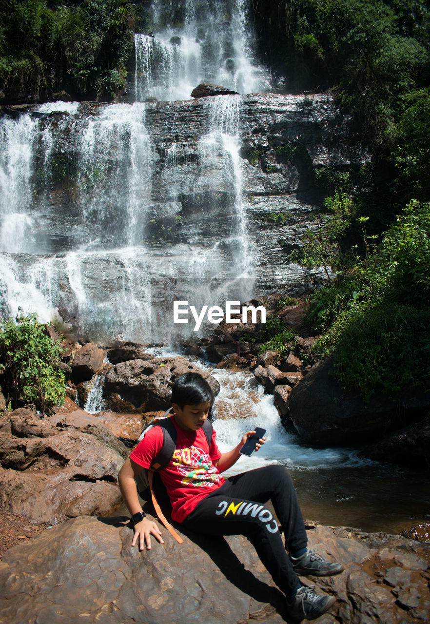 waterfall, water, rock, beauty in nature, nature, scenics - nature, motion, one person, sitting, leisure activity, full length, forest, plant, adult, tree, sports, long exposure, flowing water, land, activity, adventure, young adult, lifestyles, environment, outdoors, river, relaxation, holiday, trip, vacation, non-urban scene, body of water, day, travel, travel destinations, women, rock formation, water feature, flowing, men