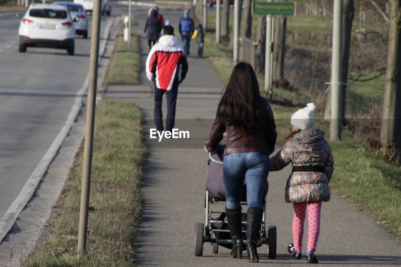 Full length rear view of mother and daughter walking on sidewalk