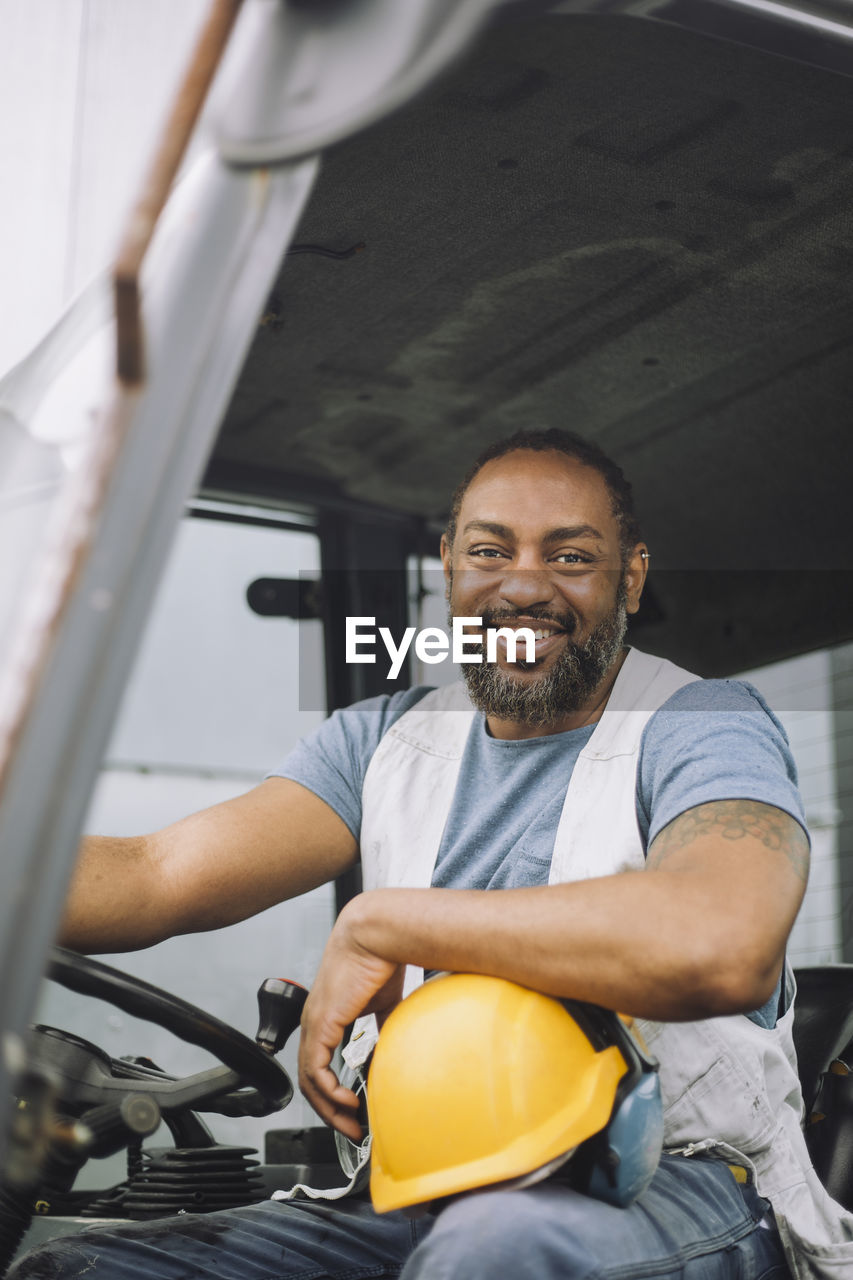 Portrait of happy mature construction worker with hardhat sitting in vehicle