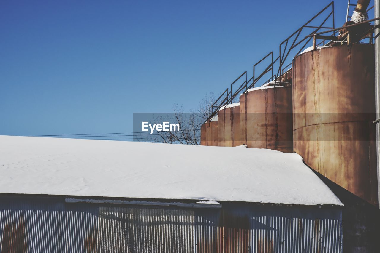 Snow covered barn by silos against clear sky