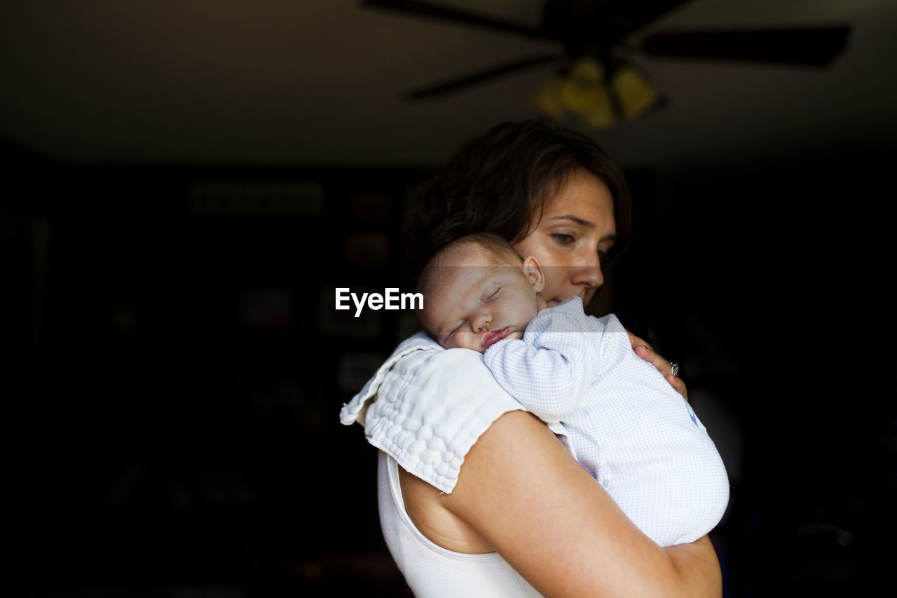 Thoughtful mother carrying baby girl while standing at home