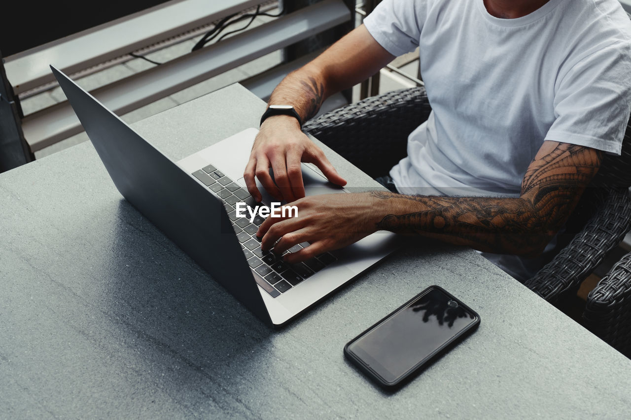 Midsection of businessman using laptop on desk in cafe